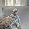 baby, bow, child, clothing, couch, curtains, cushion, happy, headband, home, indoor, infant, living_room, natural_light, patterned_pants, portrait, sitting, smiling, sofa, window