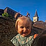 architecture, baby, blue_sky, building, child, church_tower, cute, daylight, face, green_dress, hair_ties, happy, outdoor, person, pigtails, portrait, smiling, stone_wall, sunlight, toddler