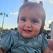 Paola participe au concours pour gagner de l'argent avec cette photo : baby, background, child, cloud, cute, daylight, face, flower_embroidery, green_clothing, hand, happy, holding, outdoor, person, pigtails, portrait, sky, smiling, street_lamp, teeth