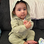 Angelica is registered to the contest to win money with this photo: baby, child, hoodie, green_clothing, sitting, couch, blanket, toy, indoor, cute, hands_clasped, foot, face, looking, expression, soft_texture, infant, cozy, portrait, casual