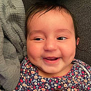 Angelica is registered to the contest to win money with this photo: baby, smile, happy, face, dimples, clothing, floral_pattern, person, child, infant, cute, portrait, indoors, soft_fabric, cushion, closeup, skin, hair, eyes, joy