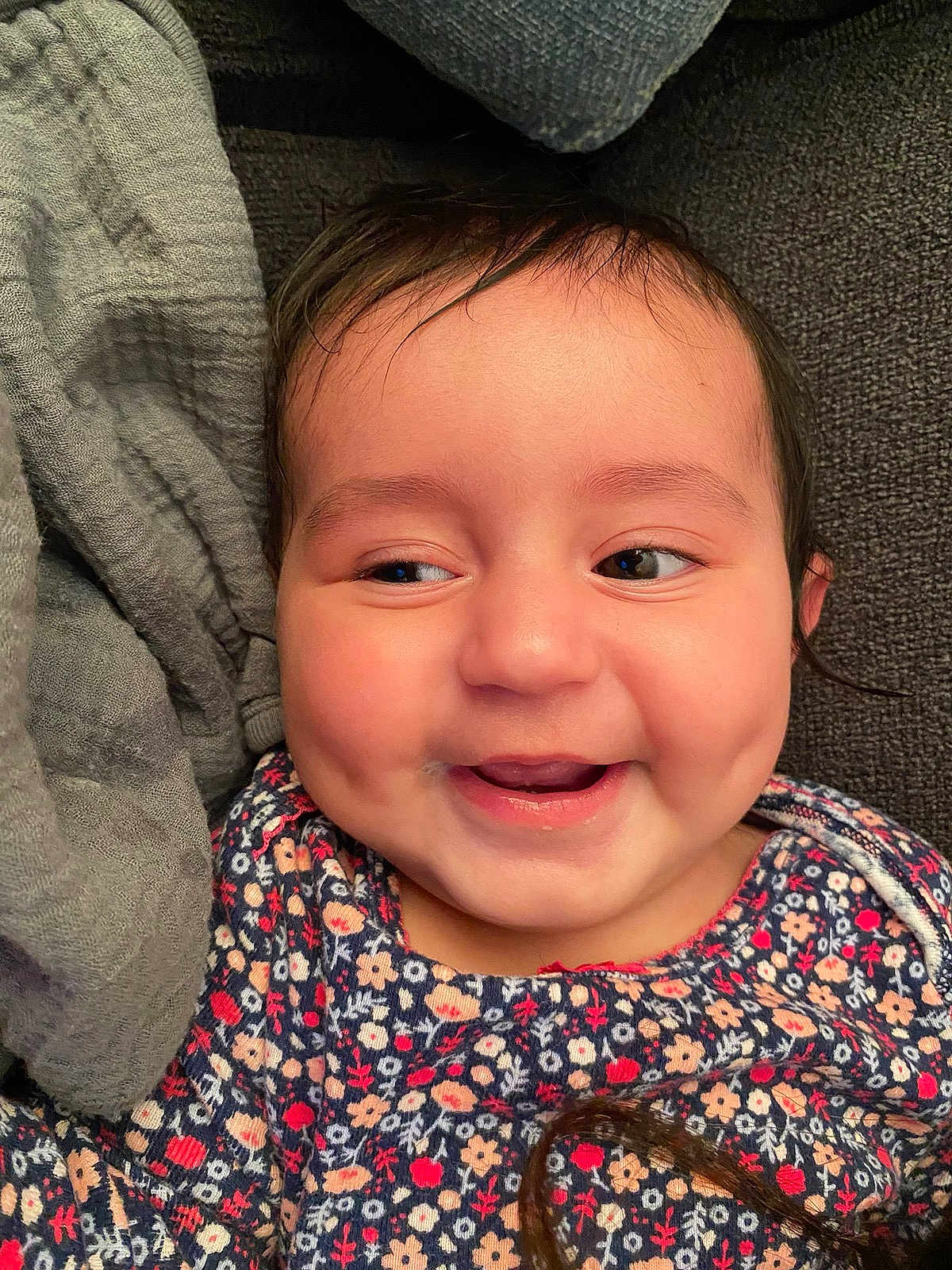 Angelica is registered to the contest to win money with this photo: baby, smile, happy, face, dimples, clothing, floral_pattern, person, child, infant, cute, portrait, indoors, soft_fabric, cushion, closeup, skin, hair, eyes, joy