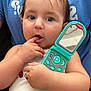 Angelica is registered to the contest to win money with this photo: baby, child, toy_phone, mirror, hand, curious, white_tank_top, ladybug, closeup, skin, face, finger_in_mouth, blue_shirt, person, infant, cute, expression, holding, indoor, portrait