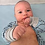 baby, infant, face, eyes, fist, hand, blue_clothing, patterned_outfit, chubby_cheeks, skin, lying_down, soft_background, curious_expression, closeup, portrait, child, cute, indoors, young, person