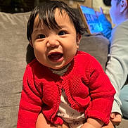 Arya is registered to the contest to win money with this photo: baby, child, red_sweater, smile, happy, indoors, couch, person, tablet, technology, knitwear, face, hand, sitting, cute, infant, portrait, warm_lighting, home, cozy