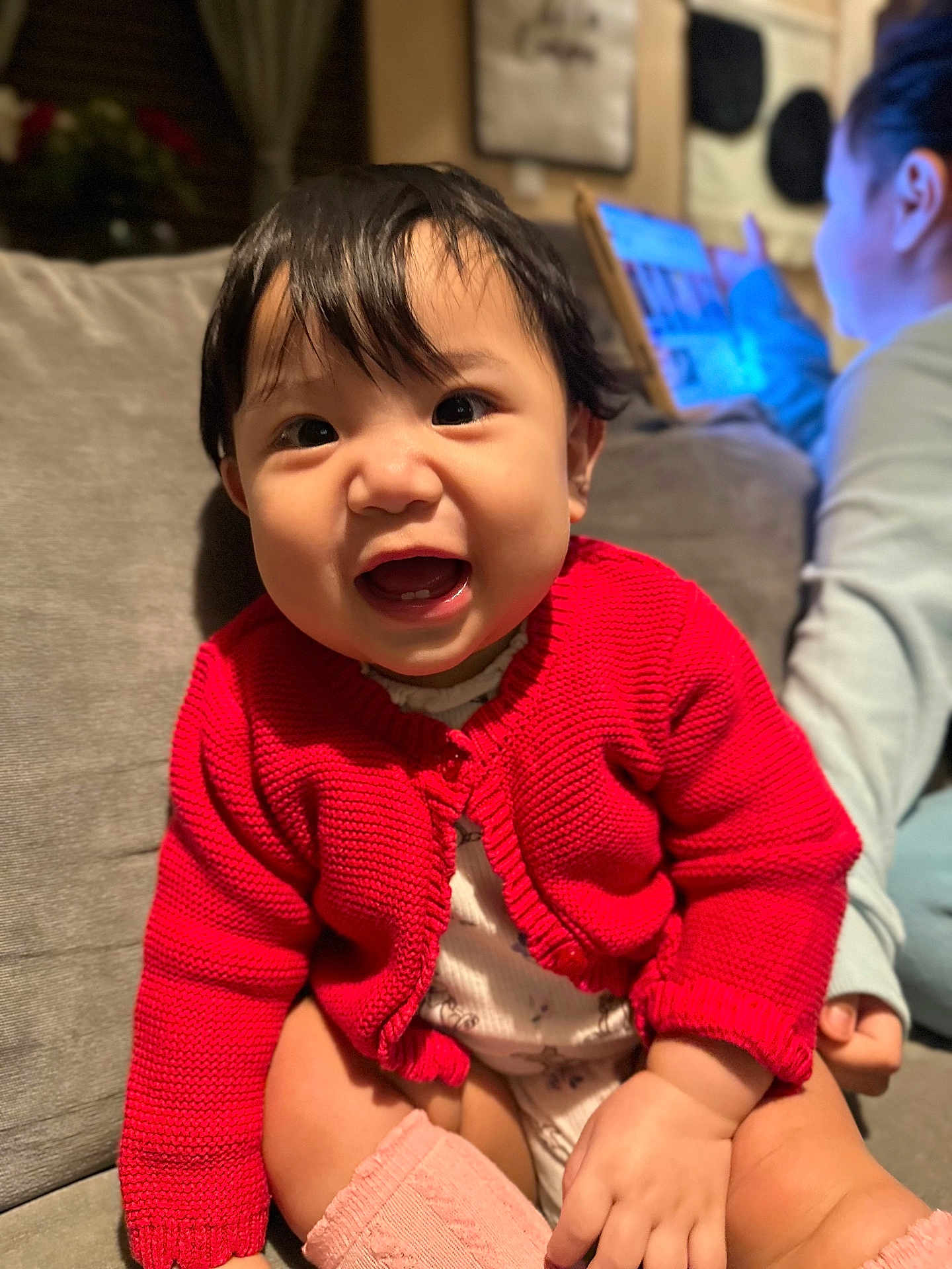 Arya is registered to the contest to win money with this photo: baby, child, red_sweater, smile, happy, indoors, couch, person, tablet, technology, knitwear, face, hand, sitting, cute, infant, portrait, warm_lighting, home, cozy