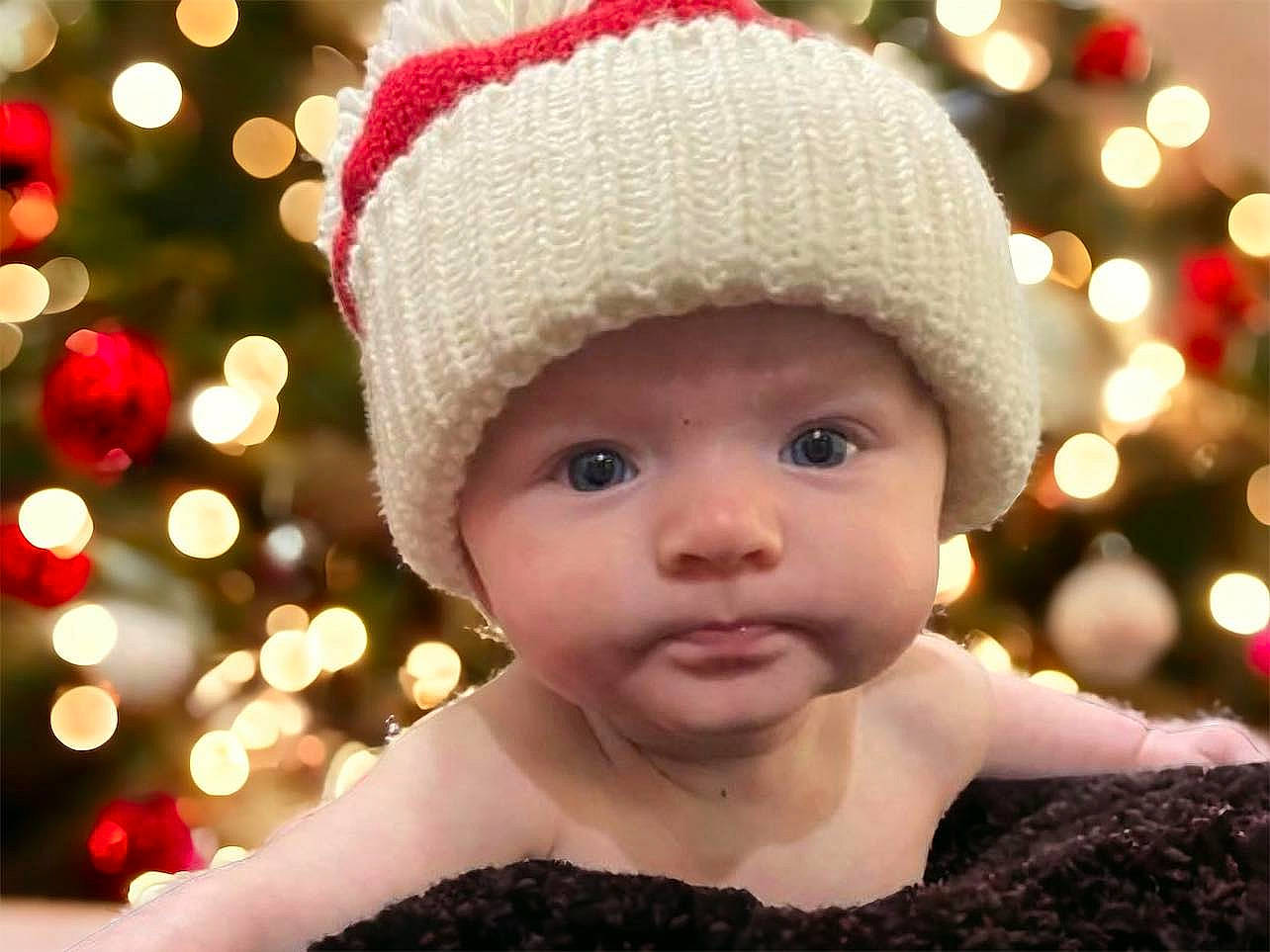 Grace is registered to the contest to win money with this photo: baby, beauty, cap, christmas_decoration, christmas_ornament, christmas_tree, costume_hat, event, eye, face, facial_expression, happy, head, headgear, headwear, holiday, human_body, light, ornament, person