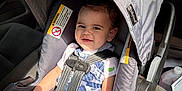 Winston is registered to the contest to win money with this photo: toddler, child, car_seat, safety_harness, sunlight, plaid_clothing, smiling, baby, seatbelt, vehicle_interior, cute, young_child, infant, casual_wear, seat, happy, portrait, indoors, car, baby_hat