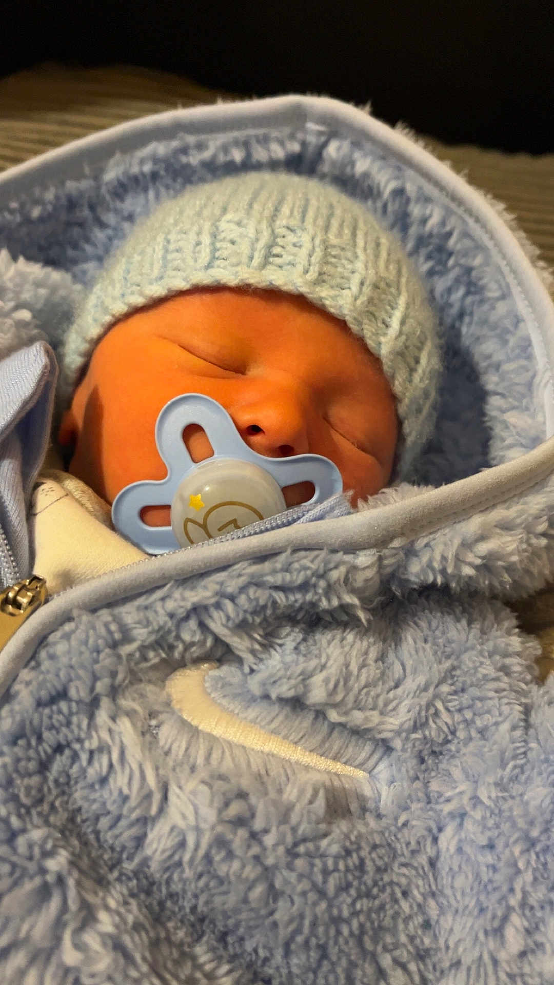 Issac is registered to the contest to win money with this photo: newborn, baby, sleeping, pacifier, hat, knitted, blue, jacket, fuzzy, cozy, infant, cute, closeup, portrait, child, warm, resting, soft, indoors, peaceful