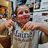 Robert is registered to the contest to win money with this photo: child, boy, smiling, thumbs_up, snack, potato_chip, food, kitchen, indoor, portrait, happy, face, hands, gray_shirt, table, refrigerator, magnets, notes, home, casual