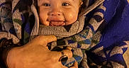 Alita is registered to the contest to win money with this photo: baby, infant, child, adult, parent, smiling, tongue_out, portrait, close_up, indoors, warm_lighting, blanket, wrapped, holding, family, face, hands, cozy, patterned_clothing, happy