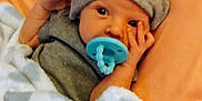 Zayden joined the competition — help win amazing prizes! baby, blanket, child, cozy, cute, face, floral_background, hat, indoors, infant, looking, lying_down, newborn, orange_cushion, pacifier, resting, sleeping_area, small_hand, soft_texture, wrapped