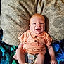 baby, blanket, child, comfort, cozy, cute, happy, indoors, infant, lying_down, orange_shirt, patterned, pillow, plaid_shorts, portrait, small_feet, small_hands, smiling, soft_lighting, young