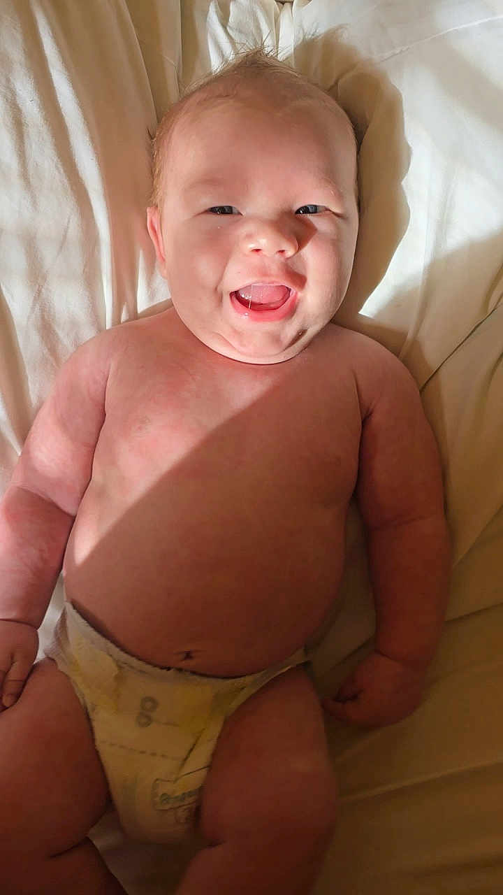 Judah joined the competition — help win amazing prizes! baby, smiling, diaper, bed, bedding, infant, happy, skin, child, cute, lying_down, light, shadow, hair, chubby, person, indoors, young, expression, closeup