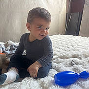 Elyano a rejoint le concours — aidez-le/la à gagner de superbes lots ! toddler, child, smiling, indoor, blanket, toy, pacifier, rattle, furniture, bed, cozy, happy, sitting, person, clothing, sock, hair, face, cute, home