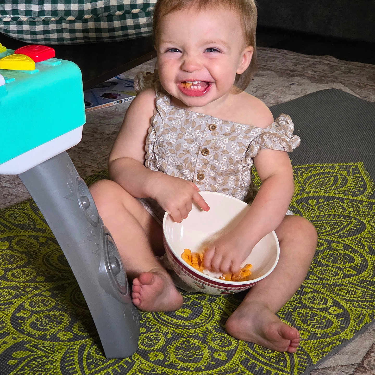Lucia is registered to the contest to win money with this photo: toddler, child, baby, smiling, happy, sitting, indoor, portrait, face, teeth, dress, bowl, snack, food, toy, playroom, rug, cushion, carpet, family_home