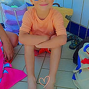 Clément a rejoint le concours — aidez-le/la à gagner de superbes lots ! child, boy, sunglasses, smiling, sitting, barefoot, tiled_floor, bag, flip_flops, orange_shirt, heart_doodle, blue_tiles, summer, casual, outdoor, person, footwear, accessory, relaxed, happy