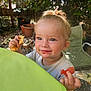 child, toddler, snack, food, face, smile, hair, blond, outdoor, garden, plants, pot, table, green, chair, happy, cute, person, messy_face, daylight