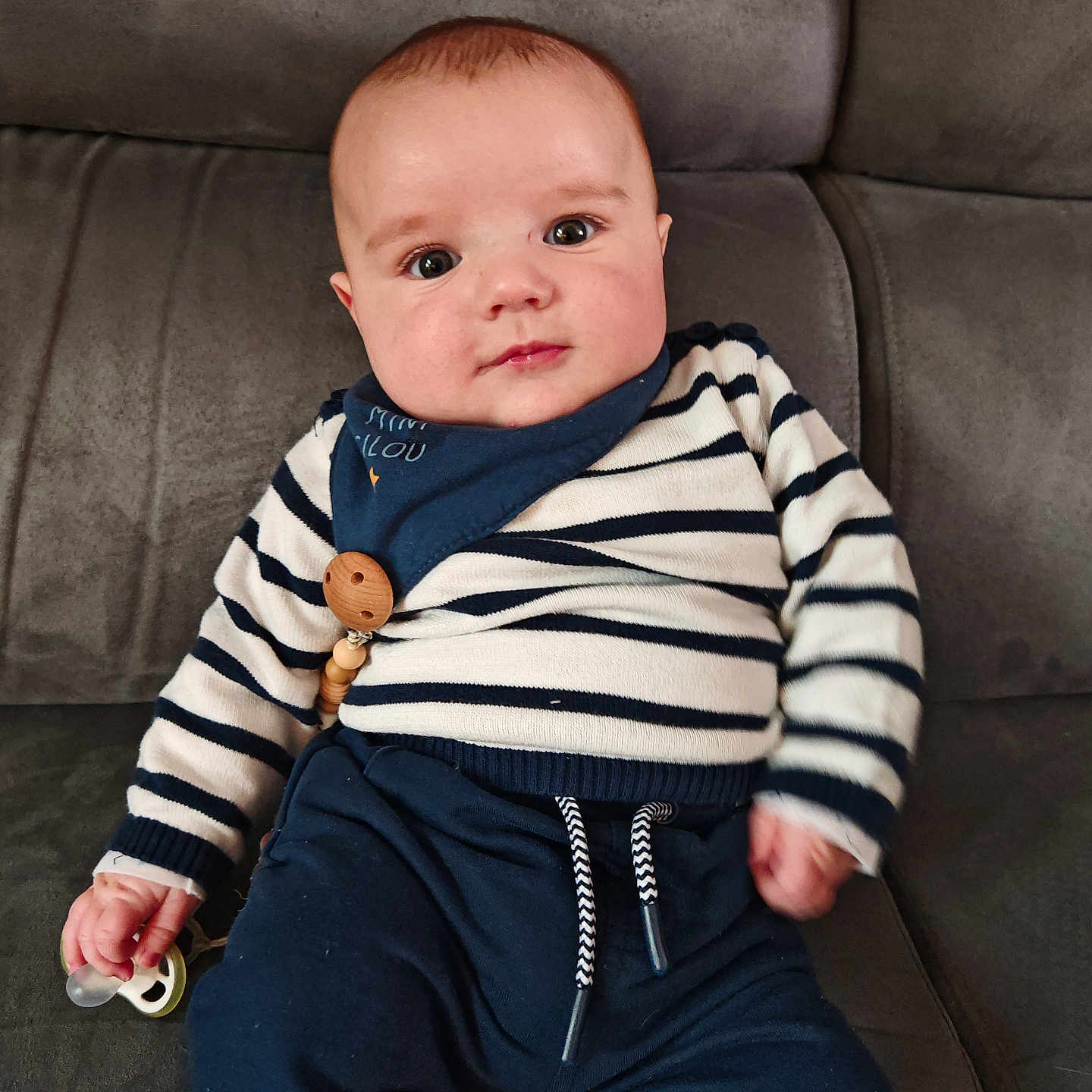 Néo a rejoint le concours — aidez-le/la à gagner de superbes lots ! baby, babysitting, blue_pants, casual_clothing, child, comfort, couch, cute, expression, face, home, indoor, infant, pacifier, person, seated, small_hand, soft_furniture, striped_clothing, young