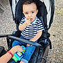 Teïva participe au concours pour gagner de l'argent avec cette photo : toddler, child, stroller, toy, snack, striped_shirt, blue_jeans, footwear, outdoor, gravel, hand, curly_hair, baby_shoes, seat, play, person, casual, expression, young_child, comfort