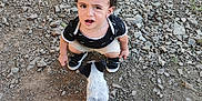 Teïva participe au concours pour gagner de l'argent avec cette photo : child, toddler, puppy, dog, rocky_ground, sneakers, shorts, black_shirt, curly_hair, outdoor, person, footwear, sandals, expression, animal, pet, grass, dirt, rocks, interaction