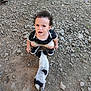 child, toddler, puppy, dog, rocky_ground, sneakers, shorts, black_shirt, curly_hair, outdoor, person, footwear, sandals, expression, animal, pet, grass, dirt, rocks, interaction