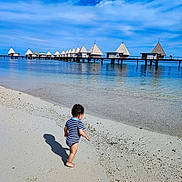 Teïva a rejoint le concours — aidez-le/la à gagner de superbes lots ! toddler, beach, sand, water, ocean, sky, clouds, pier, bungalows, vacation, summer, child, swimsuit, shadow, outdoor, nature, travel, holiday, coast, shore