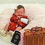 Angelika is registered to the contest to win money with this photo: baby, infant, smile, closed_eyes, bow, rust_clothing, white_shoes, passport, wicker_bag, travel, cup, metal_straw, blanket, pink_tulle, cute, sleepy, indoor, portrait, small, accessories