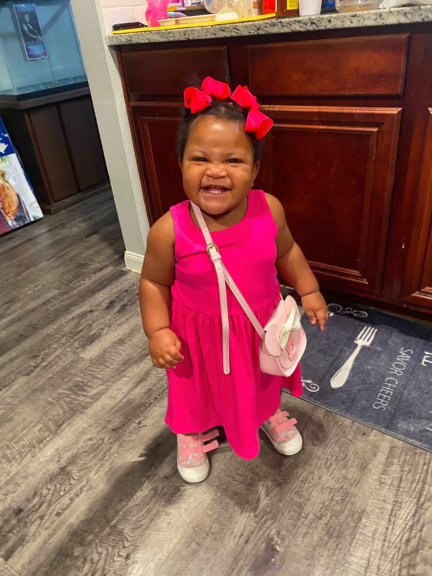 Bella joined the competition — help win amazing prizes! child, smiling, pink_dress, hair_bows, shoes, purse, indoor, floor, kitchen, cabinet, wood_floor, happy, toddler, standing, person, cute, fashion, accessory, expression, young_child