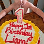 Liam is registered to the contest to win money with this photo: baby, birthday_cake, number_candle, child, wooden_chair, table, cake, icing, celebration, one_year_old, curious, indoors, home, face, person, food, dessert, colorful, happy, party