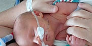 Liam is registered to the contest to win money with this photo: baby, infant, sleeping, medical_tube, hospital, adult_hand, pacifier, skin, closeup, newborn, care, healthcare, rest, comfort, person, holding, fragile, tubing, blanket, hospital_environment