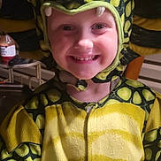 Konnor joined the competition — help win amazing prizes! child, costume, dinosaur, smile, happy, face, hood, yellow, green, indoor, person, cute, playful, childhood, fun, portrait, clothing, fancy_dress, holiday, celebration