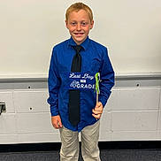 Landon is registered to the contest to win money with this photo: child, boy, classroom, celebration, last_day, 4th_grade, shirt, tie, smile, standing, holding, sign, school, indoor, young, person, pants, shoes, happy, education