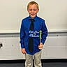child, boy, classroom, celebration, last_day, 4th_grade, shirt, tie, smile, standing, holding, sign, school, indoor, young, person, pants, shoes, happy, education