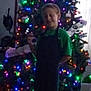 child, christmas_tree, lights, apron, green_shirt, holiday, indoor, decorations, blur, smile, festive, celebration, person, home, background, colorful, happy, seasonal, portrait, young