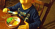 Landon joined the competition — help win amazing prizes! blue_shirt, bookshelf, bowl, boy, cake, carpet, casual_clothing, child, dessert, food, furniture, happy, home, indoor, person, room, smiling, spoon, table, wooden_chair
