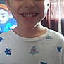 child, smiling, shirt, shark_pattern, indoor, curtain, television, cartoon, blond_hair, face, young, happy, casual_clothing, person, portrait, close_up, background, window, home, light