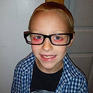 Landon is registered to the contest to win money with this photo: child, boy, glasses, smile, red_hair, blue_checkered_shirt, black_tshirt, indoor, door, wall, portrait, happy, casual_clothing, light_skin, standing, young, person, eyewear, closeup, front_view