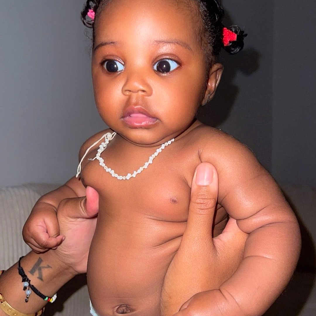 Kaëline participe au concours pour gagner de l'argent avec cette photo : baby, bracelet, child, closeup, curly_hair, cute, diaper, expression, hair_ties, hands, holding, indoor, infant, necklace, person, portrait, skin, sofa, tattoo, wide_eyes