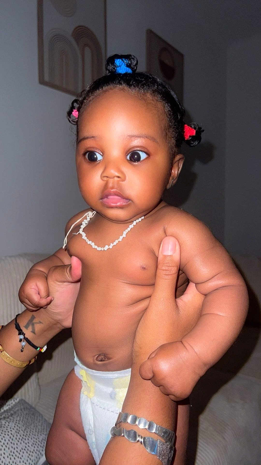 Kaëline participe au concours pour gagner de l'argent avec cette photo : baby, bracelet, child, closeup, curly_hair, cute, diaper, expression, hair_ties, hands, holding, indoor, infant, necklace, person, portrait, skin, sofa, tattoo, wide_eyes