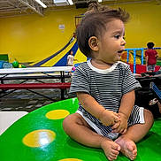 Amadeo joined the competition — help win amazing prizes! toddler, child, striped_clothing, indoor, play_area, table, green_table, yellow_spots, slide, kids, background, floor, bench, short_hair, curious, seated, cross_legged, expression, playground, colorful