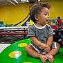 toddler, child, striped_clothing, indoor, play_area, table, green_table, yellow_spots, slide, kids, background, floor, bench, short_hair, curious, seated, cross_legged, expression, playground, colorful