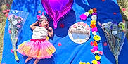 Nyra Adithi Darshan joined the competition — help win amazing prizes! baby, child, birthday, cake, balloon, flower_bouquet, grass, blanket, tutu, unicorn_headband, yawning, pink, purple, blue, outdoor, celebration, petals, sunlight, cute, festive