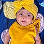 baby, infant, yellow_headband, yellow_clothing, knitted_bow, blue_blanket, patterned_blanket, child, portrait, face, eyes, cute, smiling, lying_down, indoors, closeup, skin, headwear, expression, sleepwear