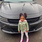 Riley joined the competition — help win amazing prizes! child, girl, car, black_car, dodge, parking_lot, rain, sidewalk, jacket, hoodie, leggings, sneakers, pink_shoes, hair_buns, outdoor, daytime, curious, standing, vehicle, urban