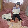 child, boy, smile, sign, announcement, pregnancy_test, ultrasound, pink_fabric, barefoot, baby_clothes, handwritten, sitting, indoor, window, curtain, happy, family, brother, sister, celebration