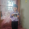 child, boy, smiling, ultrasound_photo, window, curtain, snowflake_decorations, purple_shirt, black_pants, indoor, happy, portrait, standing, light_switch, sheer_fabric, sparkle, home, decor, person, cute