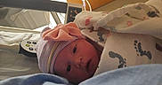 Chelsea joined the competition — help win amazing prizes! newborn, baby, hospital, blanket, hat, bed, medical_equipment, infant, person, face, headwear, wrapped, footprints, pink, striped, curious, lying_down, indoors, patient, newborn_baby
