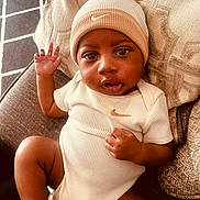 Damoni joined the competition — help win amazing prizes! baby, infant, child, onesie, hat, beige_clothing, couch, pillow, hand, foot, face, smiling, indoors, relaxing, texture, pattern, nike_logo, portrait, cute, waving