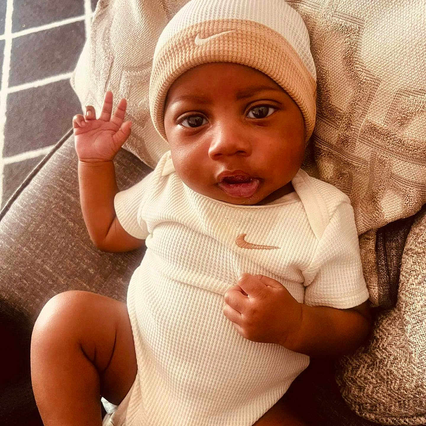 Damoni joined the competition — help win amazing prizes! baby, infant, child, onesie, hat, beige_clothing, couch, pillow, hand, foot, face, smiling, indoors, relaxing, texture, pattern, nike_logo, portrait, cute, waving